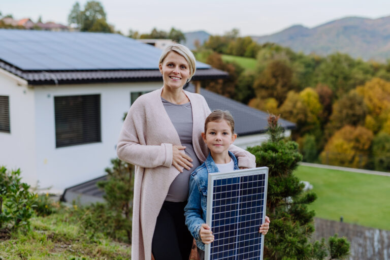 Mère avec sa petite fille près de leur maison avec des panneaux solaires. Énergie alternative, économies