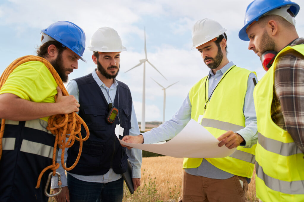 Groupe d'ingénieurs discutant et travaillant sur un plan dans un champ agricole avec des éoliennes