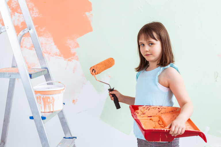 Réparation dans l'appartement. Happy Child Girl peint le mur avec de la peinture orange. Rénovation